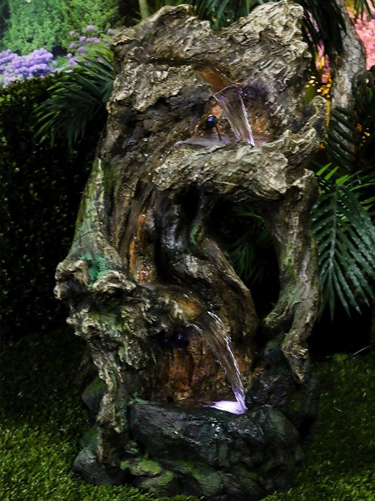 Tree trunk fountain with LED lights, close-up view.